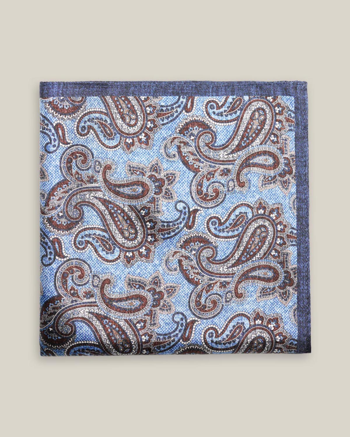 Light-blue printed silk pocket square with large brown, ivory and deep blue paisley motifs and a contrasting navy border.