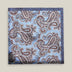 Light-blue printed silk pocket square with large brown, ivory and deep blue paisley motifs and a contrasting navy border.
