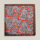 Rust-red printed silk pocket square with large brown, ivory and muted blue paisley motifs and a contrasting brown border.