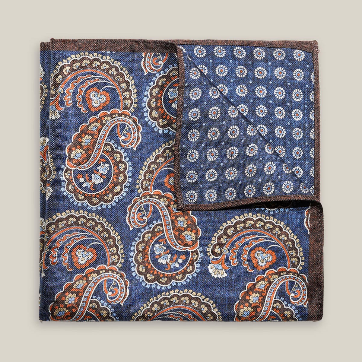 Navy double-face silk pocket square with ornate brown, orange and ivory paisley, a small floral medallion reverse and a brown border.