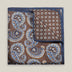 Brown double-face silk pocket square with ornate pale blue, navy, ochre and ivory paisley, a small floral medallion reverse and a navy border.