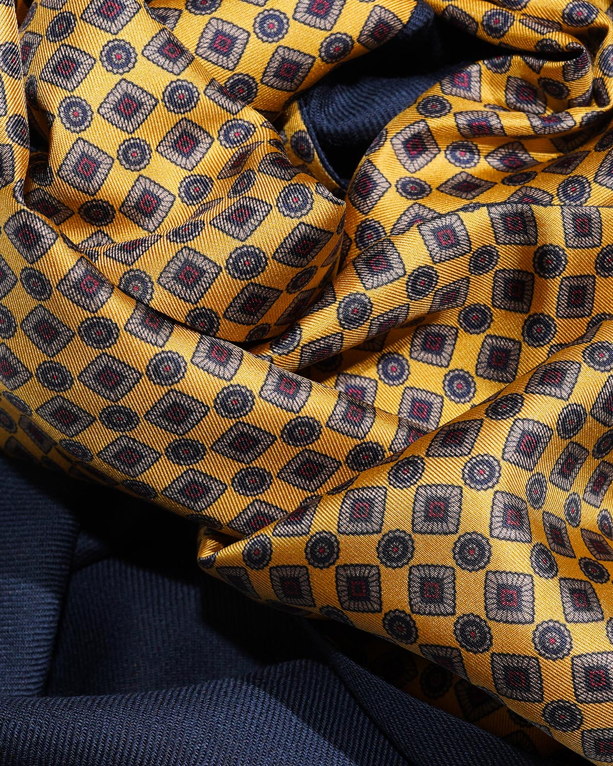 Draped golden geometric printed silk with burgundy accents alongside the scarf's navy wool backing