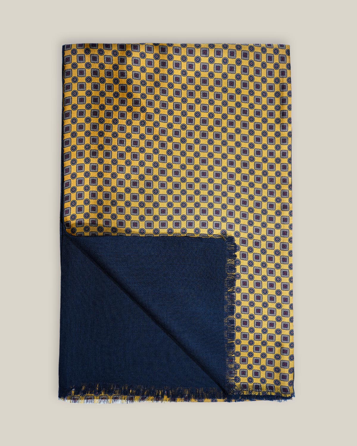 Golden-yellow geometric printed silk scarf folded to show its plain navy wool backing and short fringed edges