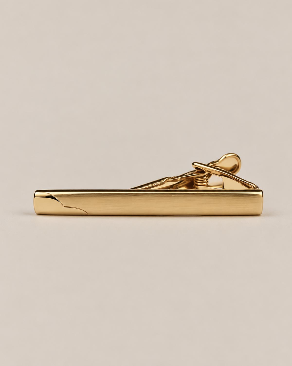 Gold-tone tie clip with a smooth reflective face, curved detail at one end and spring-loaded fastening.