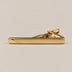 Gold-tone tie clip with a smooth reflective face, curved detail at one end and spring-loaded fastening.