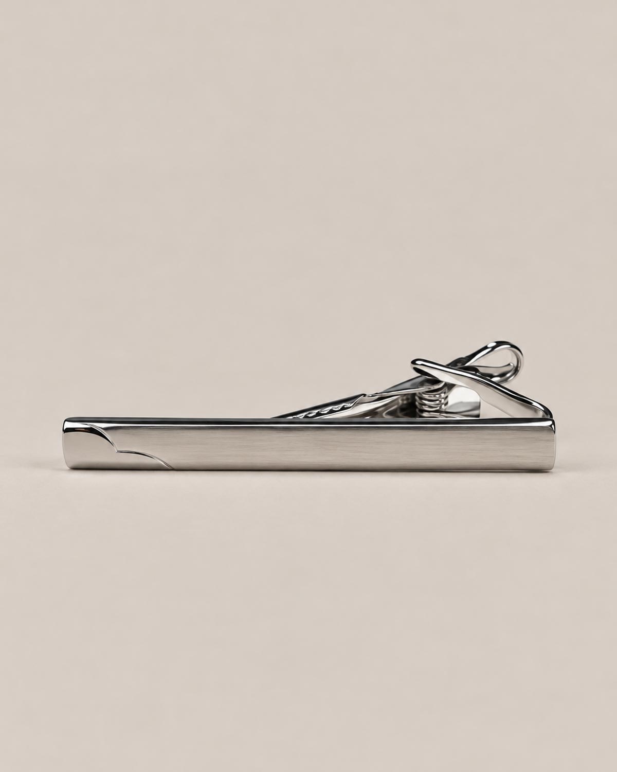 Silver-tone tie clip with a smooth reflective face, curved detail at one end and spring-loaded fastening.