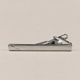Silver-tone tie clip with a smooth reflective face, curved detail at one end and spring-loaded fastening.