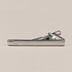 Silver-tone tie clip with a smooth reflective face, curved detail at one end and spring-loaded fastening.