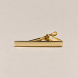 Shiny gold-tone tie clip with a smooth straight front and spring-loaded fastening.