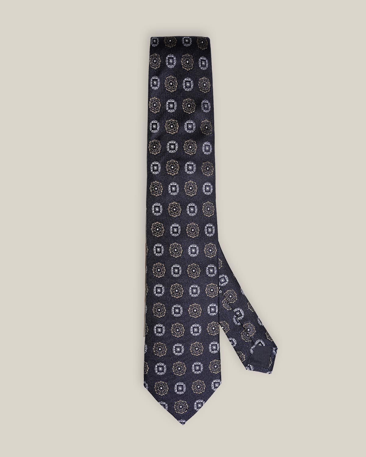 Navy woven silk tie with repeating silver-toned geometric medallions on a light background