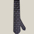 Navy woven silk tie with repeating silver-toned geometric medallions on a light background