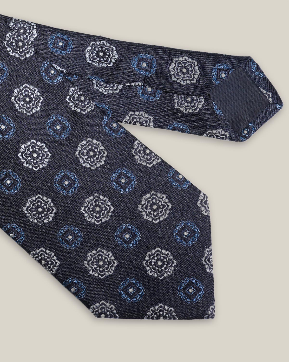 Navy woven silk tie with repeating light blue and silver-toned geometric medallions
