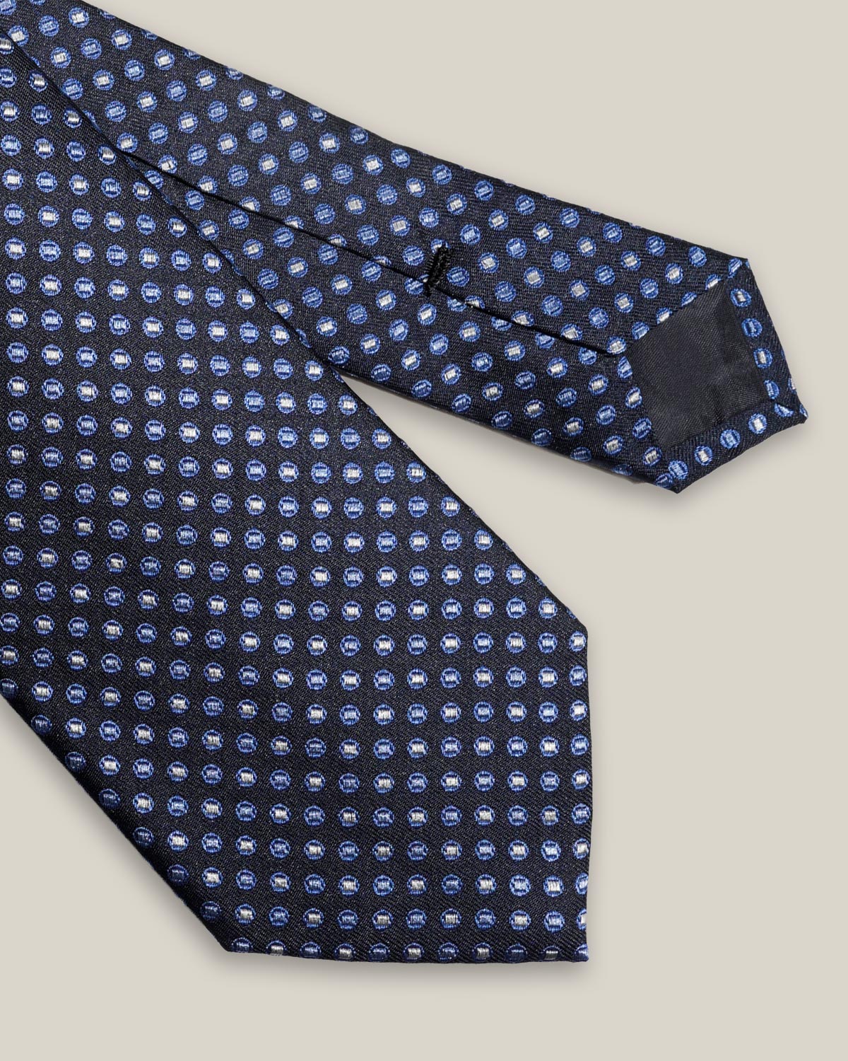 Close-up of the navy silk tie showing light blue and ivory medallions and the pointed blade.