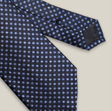 Close-up of the navy silk tie showing light blue and ivory medallions and the pointed blade.