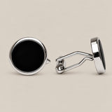 Round silver cufflinks with a deep black onyx face on a beige background