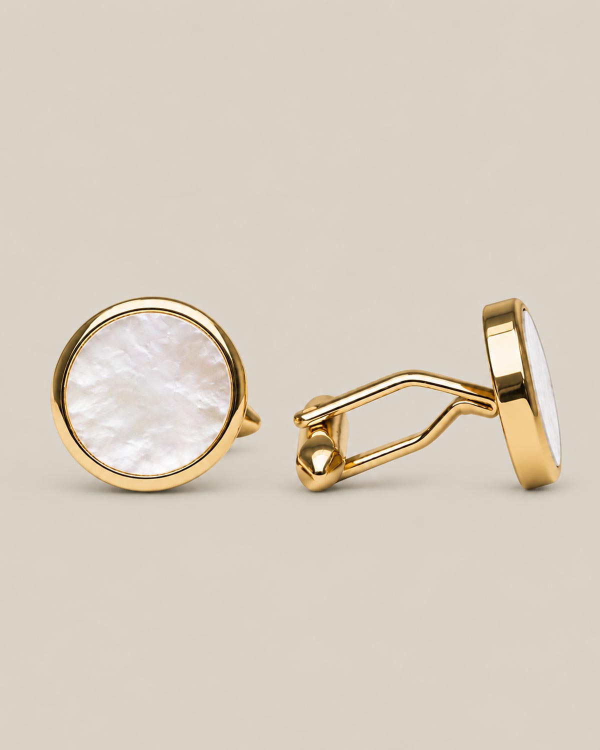 Round gold cufflinks with white mother of pearl face on a beige background