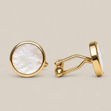 Round gold cufflinks with white mother of pearl face on a beige background