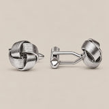 Silver love knot cufflinks in polished woven wire on a beige background