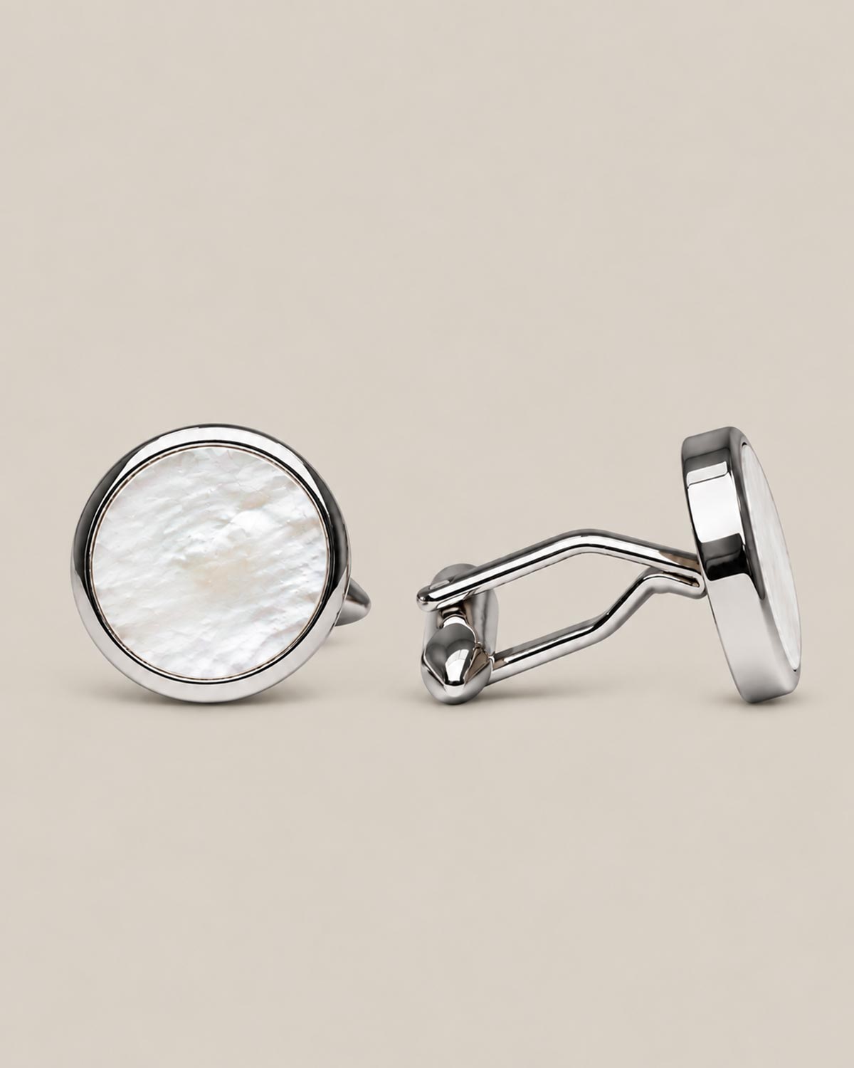 Round silver cufflinks with white mother of pearl face on a beige background