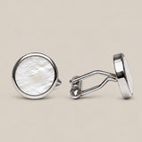 Round silver cufflinks with white mother of pearl face on a beige background