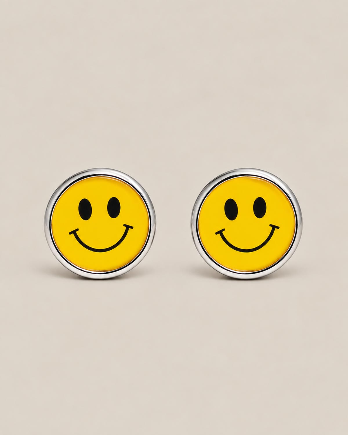 Round silver cufflinks with yellow smiley face enamel motif on a beige background