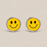 Round silver cufflinks with yellow smiley face enamel motif on a beige background